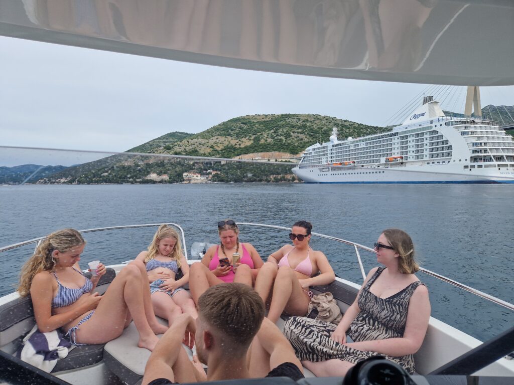 Rent boat Dubrovnik private group enjoying Adriatic coastline views with luxury cruise ship in background